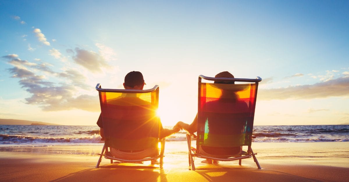 Retired couple relaxing during sunset on the beach in lounge chairs