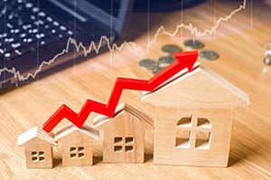 A red arrow above the wooden houses up. Concept of increasing costs of housing and need for more affordable housing.