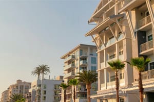 Row of apartment buildings with glass railings on the balconies at Oceanside, California. Exterior of buildings with light wall claddings and palm trees at the front.