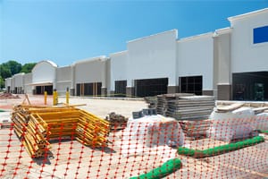 A retail shopping center construction site fenced off by orange netting.  Construction supplies are stacked in the parking lot.